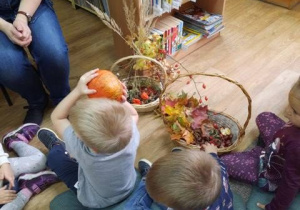 Dzieci siedzą na poduszkach w bibliotece oglądając dary jesieni